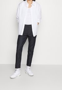 White button-up shirt over a white tank top, paired with dark blue jeans and white sneakers. Smooth fabric and casual fit.