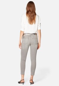 Jeans ajustados grises de mezclilla, con un ajuste slim y detalles decorativos en los bolsillos traseros, combinados con una blusa blanca y tacones negros.
