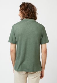 Grünes kurzärmeliges Polohemd mit kragenlosem Ausschnitt, weicher Textur und geradem Saum, das ein dezentes meliertes Muster aufweist.