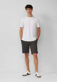 White short-sleeve t-shirt paired with dark gray shorts. The shorts have a relaxed fit and are knee-length. Footwear is white with black accents.
