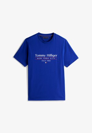 T-shirt di cotone blu con testo "Tommy Hilfiger," "NEW YORK CITY," e "Dal 1985" in bianco e rosso. Maniche corte e scollatura a girocollo.