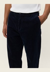 Pantaloni din corduroy bleumarin cu nervuri verticale, cu închidere prin buton, buzunare laterale și o croială lejeră. Material moale, texturat.