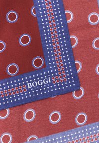 Raudonos šilkinės servetėlės su baltais ir mėlynais apvaliais raštais ir mėlynu kraštu, kuriame yra raudoni ir balti taškai bei tekstas "Bogli Milano".