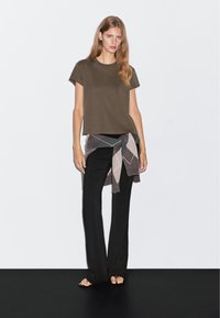 Brązowy t-shirt z krótkim rękawem w połączeniu z czarnymi spodniami o szerokich nogawkach oraz brązowym, beżowym paskiem w diamentowy wzór związanym w talii.