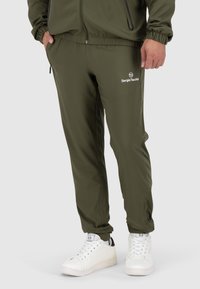 Olijfgroene sportbroeken met een elastische tailleband en ritszakken, gecombineerd met witte sneakers. Bevat een logo op de linkerdij.