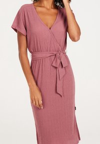 Robe portefeuille rose poussiéreux à manches courtes, tissu texturé, encolure en V, détail de ceinture à nouer et fente latérale pour faciliter les mouvements.