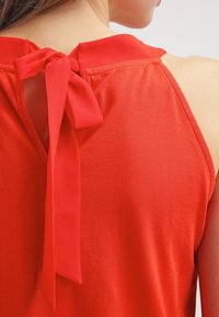 Top rosso senza maniche con un dettaglio annodato sul retro del collo. Realizzato in un tessuto morbido con una texture liscia e una vestibilità comoda.