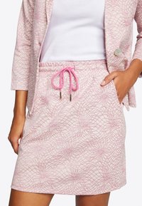 Gonna rosa chiaro con una trama testurizzata caratterizzata da linee incrociate e esplosioni di stelle. Include una vita con cordoncino rosa e tasche laterali.