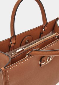Borsa a mano in pelle marrone con doppi manici, hardware in tonalità oro e scomparto con zip. Finitura texture con dettagli cuciti.