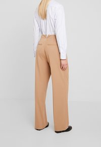 Beżowe spodnie o szerokich nogawkach, z gładkim wykończeniem, dwoma tylnymi kieszeniami i średnim stanem, w połączeniu z jasnoniebieską koszulą w paski.