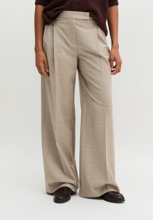 Beige wijde broeken met plooien aan de voorkant, gedragen met donkerbruine schoenen en een donkerbruine top, getoond van taille tot voeten.