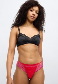 Μαύρο σατέν bralette με δαντελένιο τελείωμα και ρυθμιζόμενους ιμάντες, σετ με κόκκινο δαντελένιο στρινγκ με ανθικά σχέδια και διαφανείς λεπτομέρειες.