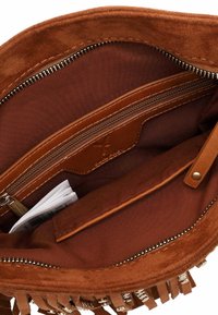Interior de un bolso de ante marrón que incluye un bolsillo con cremallera, forro de tela lisa y un pequeño folleto visible. Destaca el detalle de flecos en el exterior.
