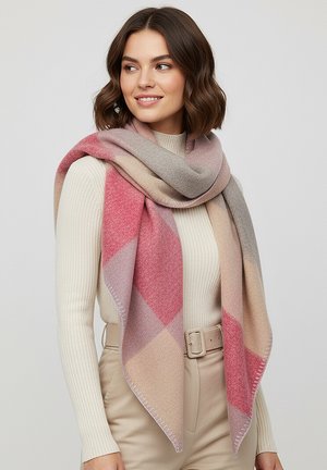 Woman with wavy brown hair wearing a cream ribbed sweater, beige belted pants, and a large pink, beige, and gray checkered scarf draped over shoulders.