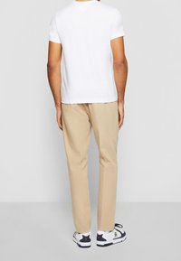 White short-sleeve t-shirt, beige trousers, and black and white sneakers. Simple design with no patterns, relaxed fit, and light texture.
