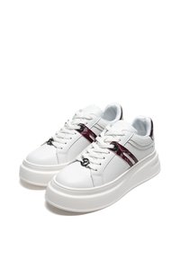 Bílé kožené tenisky s robustní podrážkou, doplněné červeným vzorovaným pruhem a černými logovými akcenty na bocích a tkaničkách.