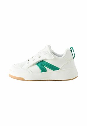 Baltas kurpes ar zaļu sānu svītru, daļēji vaļējas baltas šņores un bēša gumijas zole, izolētas uz balta fona.