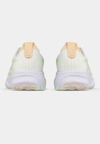 Zapatillas deportivas blancas con una parte superior lisa y texturizada, una lengüeta del talón en amarillo pastel y detalles verdes. Suela acolchada y suela exterior de goma.