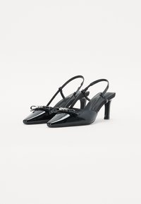 Črne lakirane slingback pete s ostrimi prsti, majhnim lokom na detajlu in tankimi petami. Gladka tekstura in sijoč zaključek.