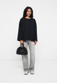 Μαύρη oversized μπλούζα με φαρδιές μανσέτες, γκρι κομψά παντελόνια και μια μικρή μαύρη τσάντα με κορδόνι. Λευκά slip-on παπούτσια με καουτσούκ σόλες.