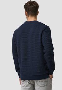 Marineblauwe sweatshirt met textuur, voorzien van een ronde hals, ribgebreide boorden en zoom. Het materiaal heeft een bubbels patroon en een gladde binnenafwerking.