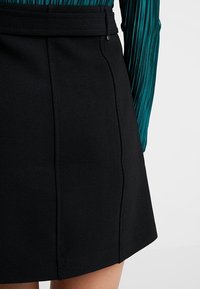 Jupe noire en ligne A dotée d'un tissu lisse et structuré avec une taille définie et des détails de couture subtils, créant une silhouette épurée.