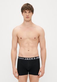 Mustat bokserit, joissa on vyötärö nauha, johon on painettu valkoisella tekstillä "JACK & JONES". Kangas näyttää pehmeältä ja istuu tiukasti.