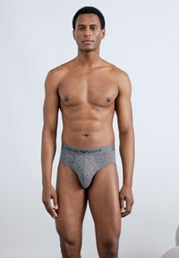 Γκρι εσώρουχα Emporio Armani με υφασμένη υφή και ελαστική μέση. Το μοντέλο ποζάρει με πρόσωπο προς τα εμπρός, με λεία υφή δέρματος.