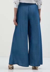 Pantaloni in denim a gamba larga di colore blu scuro, con una vita elasticizzata e una texture liscia e leggera. Senza tasche visibili o decorazioni.