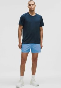 Dunkelblaues, kurzärmeliges Sportshirt aus strukturiertem Stoff, kombiniert mit hellblauen Shorts. Weiße Sportschuhe und Socken runden das Outfit ab.