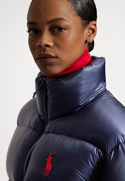 Navy puffer jacket with a high collar, featuring a red zipper and red inner lining. Red logo detailing on the chest. Smooth, glossy texture.