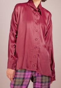 Saty, bordó košile s dlouhým rukávem a špičatým límcem, se šesti předními knoflíky; v kombinaci s kostkovanými kalhotami v různých barvách se fialovými odstíny.