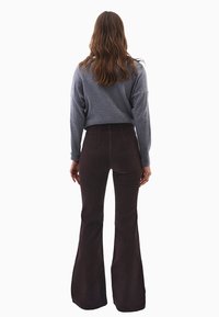 Szary sweter z długim rękawem zestawiony z brązowymi spodniami w stylu dzwonów, wykonanymi z miękkiego materiału. Szczegółowe przeszycia na spodniach. Prosty i funkcjonalny design.