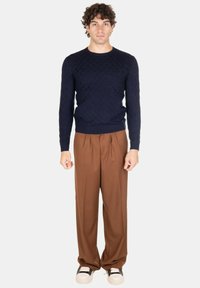 Maglione blu strutturato con colletto rotondo, abbinato a pantaloni marroni plissettati. Sneakers in bianco e nero completano l'outfit.