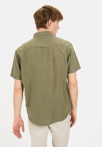 Olijfgroene shirt met korte mouwen, gemaakt van lichte stof. Voorzien van een kraag en een subtiele textuur, met een rechte zoom aan de achterkant.