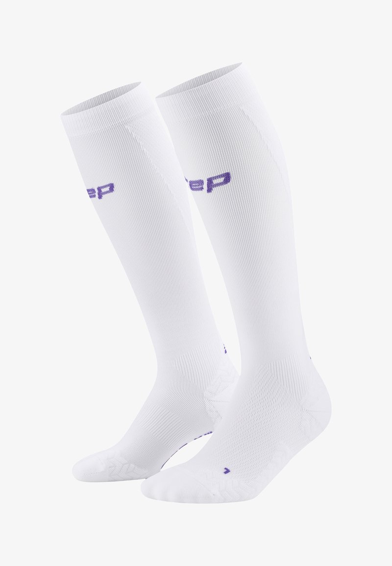 Weiße knielange Socken mit gerippter Textur, verstärktem Fersen- und Zehenbereich und einem lila Logo. Glattes Material, entworfen für Komfort und Unterstützung.