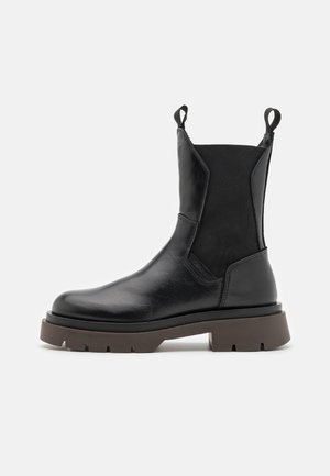 Schwarze Leder-Stiefelette mit elastischen Seitenpanelen, runder Zehenpartie und einer stabilen braunen Gummisohle. Verfügt über Zugschlaufen für ein einfaches Anziehen.