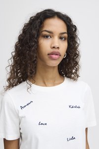 Camiseta de algodón blanca con mangas cortas, que presenta las palabras bordadas "Amour", "Kärlek", "Love" y "Liebe" en un estilo de escritura azul.