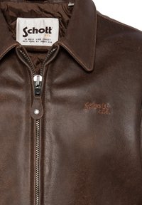 Chaqueta de cuero marrón con cierre de cremallera, cuello tipo punto y forro acolchado. El logo "Schott NYC" está grabado en el pecho.