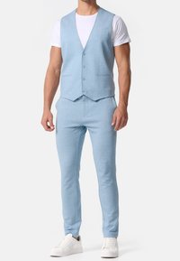 Světle modrá přiléhavá vesta z texturované látky s výstřihem do V a pěti knoflíky, doplněná o odpovídající úzké kalhoty a bílé tenisky.