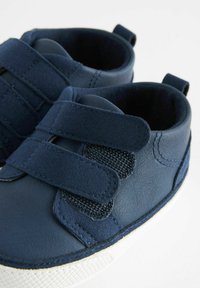 Chaussures bleu marine en cuir dotées de deux straps en velcro, d'une surface texturée et d'une semelle en caoutchouc blanche. Elles présentent un panneau en maille sur le côté pour plus de respirabilité.