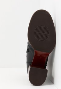 Suela de zapato de cuero negro con goma texturizada, punta redondeada y un logo circular. Presenta un acento marrón y la talla 37 marcada.