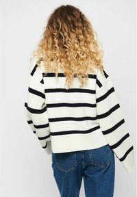 Der Strickpullover hat horizontale schwarz-weiße Streifen, einen kastenförmigen Schnitt und weite Ärmel. Kombiniert mit hoch taillierten blauen Jeans.