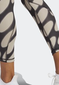 Leggings con un patrón negro y beige que presenta grandes formas curvas. La tela tiene una textura suave e incluye costuras en contraste.