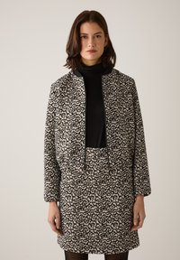 Schwarz-cremefarben gemusterte Jacke mit passendem Rock, mit kurzem Schnitt, Reißverschluss und strukturierter Stoffqualität. Lange Ärmel inklusive.