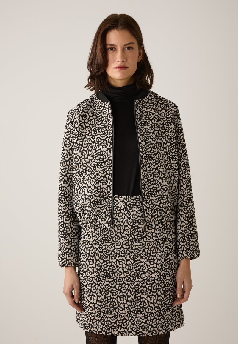 Schwarz-cremefarben gemusterte Jacke mit passendem Rock, mit kurzem Schnitt, Reißverschluss und strukturierter Stoffqualität. Lange Ärmel inklusive.