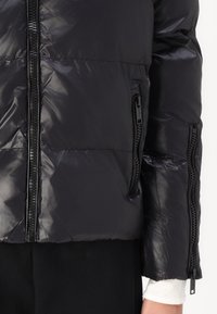 Black puffer jacket with a shiny finish, zippered front and side pockets. Features a quilted design and elastic cuffs.