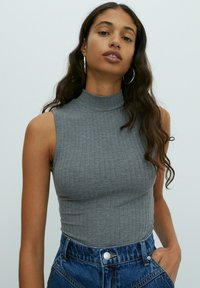 Gray ribbed sleeveless turtleneck top with a fitted design, paired with high-waisted denim shorts featuring a button closure and pockets.
