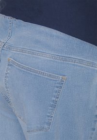 Jeans de denim azul claro com um design simples, apresentando costuras visíveis nos bolsos traseiros e uma textura lisa, ligeiramente desgastada.