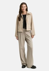 Beżowa kurtka na guziki wykonana z miękkiej tkaniny, zestawiona z szerokimi beżowymi spodniami. Całość dopełniają czarne buty na platformie.